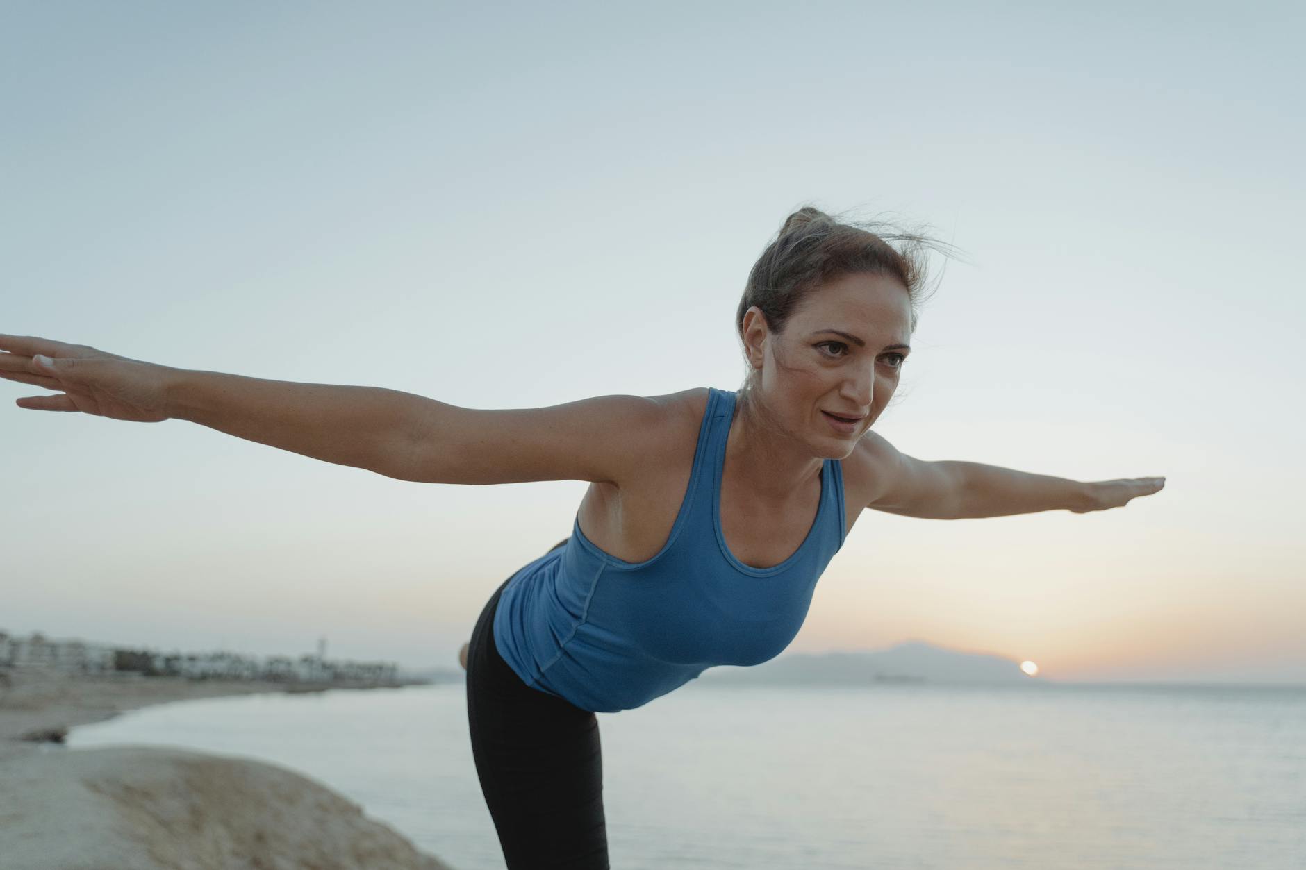 Woman performing a gentle yoga pose on a beach at sunrise.